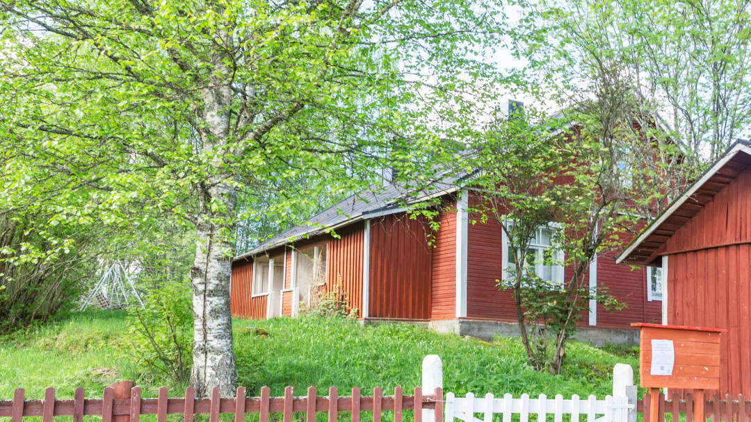 Mäkisessä pihapiirissä puinen museotalo ja piharakennus. Kuvan edustalla lauta-aita ja portti.
