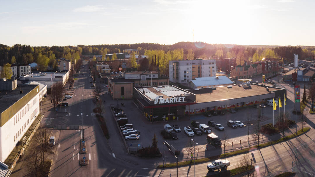 Kesäinen panoraamakuva Suonenjoen keskustasta Rautalammintien ja Iisvedentein risteyksestä. Autoja on pysäköitynä S-Marketin pihalla. Aurinkoinen kesäiltapäivä.