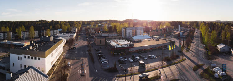 Kesäinen panoraamakuva Suonenjoen keskustasta Rautalammintien ja Iisvedentein risteyksestä. Autoja on pysäköitynä S-Marketin pihalla. Aurinkoinen kesäiltapäivä.