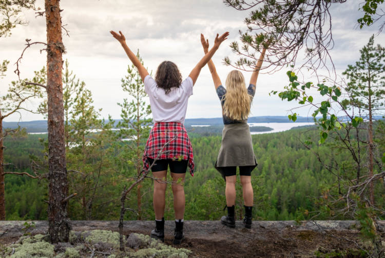Kaksi naista seisoo kallion reunalla kädet ylhäällä Kalajanvuorella.