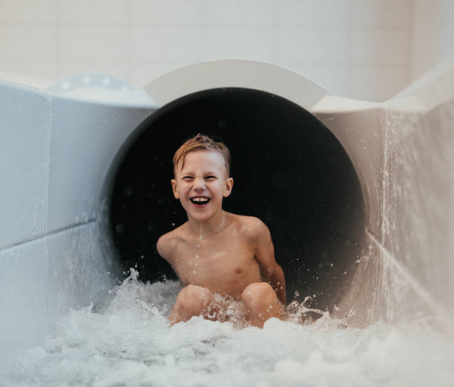 A child goes down a water slide laughing.
