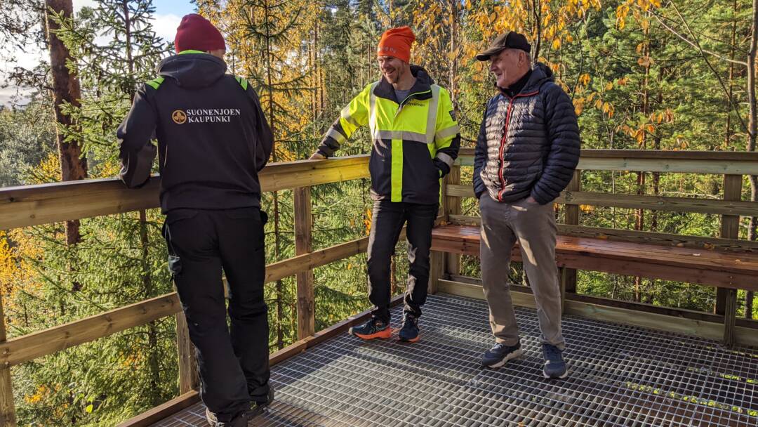 Kolme miestä seisoo kuntoportaiden tasanteella juttelemassa.