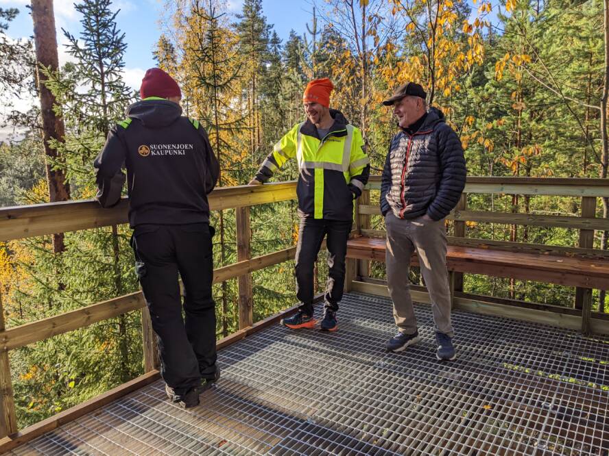 Kolme miestä seisoo kuntoportaiden tasanteella juttelemassa.