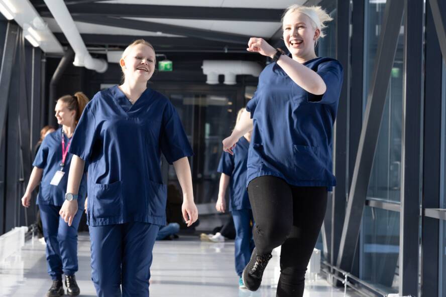 Hoitaja-opiskelijoita kävelee nauraen koulun käytävällä.
