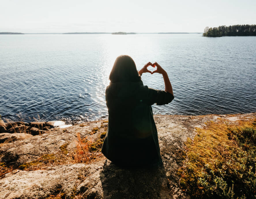 Rannalla vastavalossa istuu henkilö, joka muodostaa käsillään sydämen.