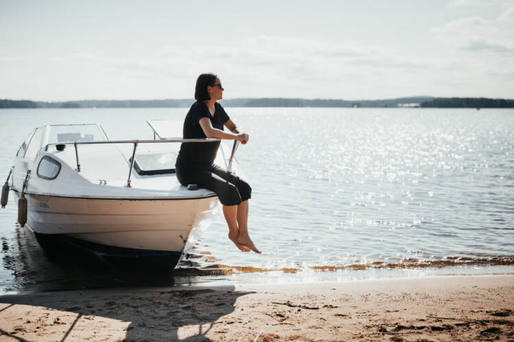 nainen istuu veneen nokassa ja katselee kaunista järvimaisemaa